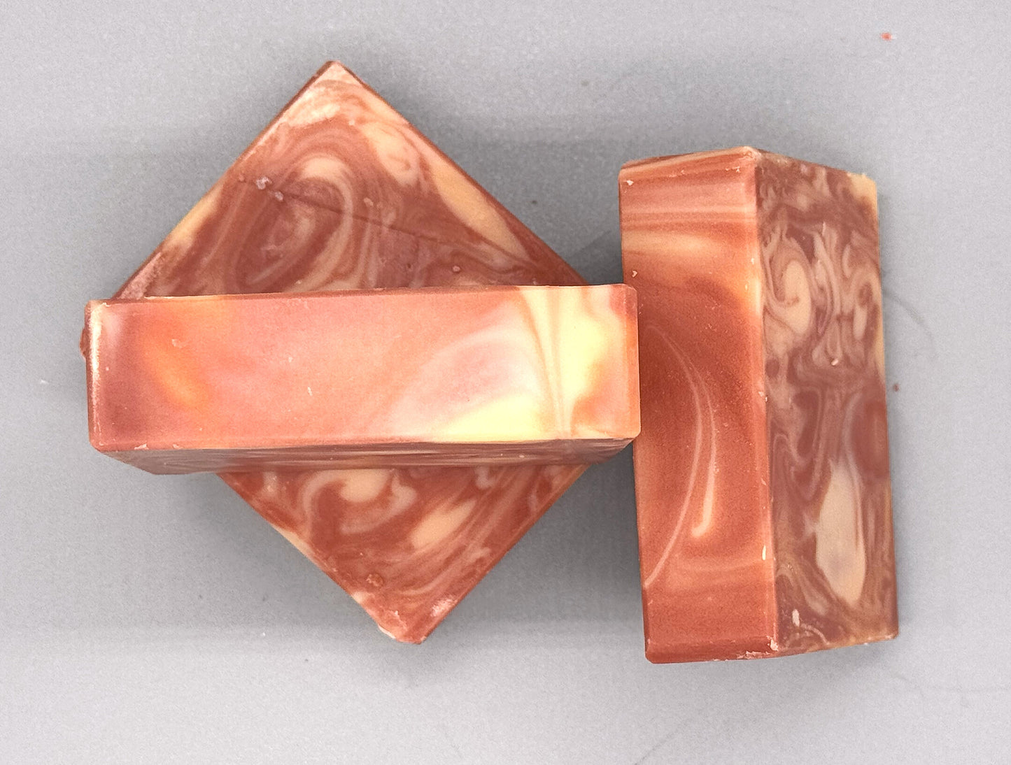 Three handmade pink and cream marbled soaps arranged on a gray surface, highlighting the unique swirls and smooth texture.