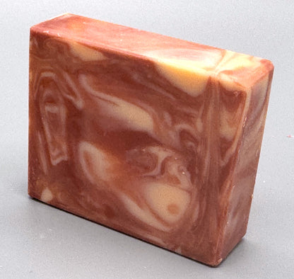 Handmade pink and cream swirled bar soap with warm, marbled tones, standing upright on a gray background