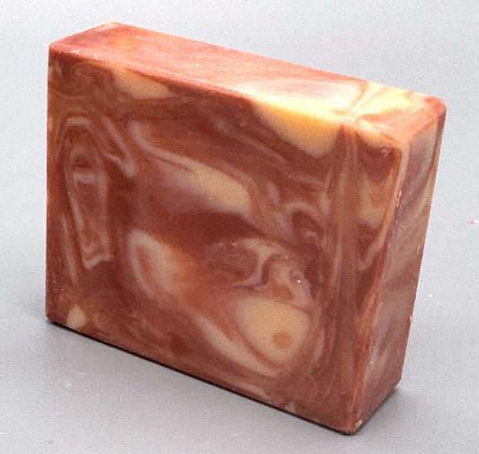 Handmade pink and cream swirled bar soap with warm, marbled tones, standing upright on a gray background