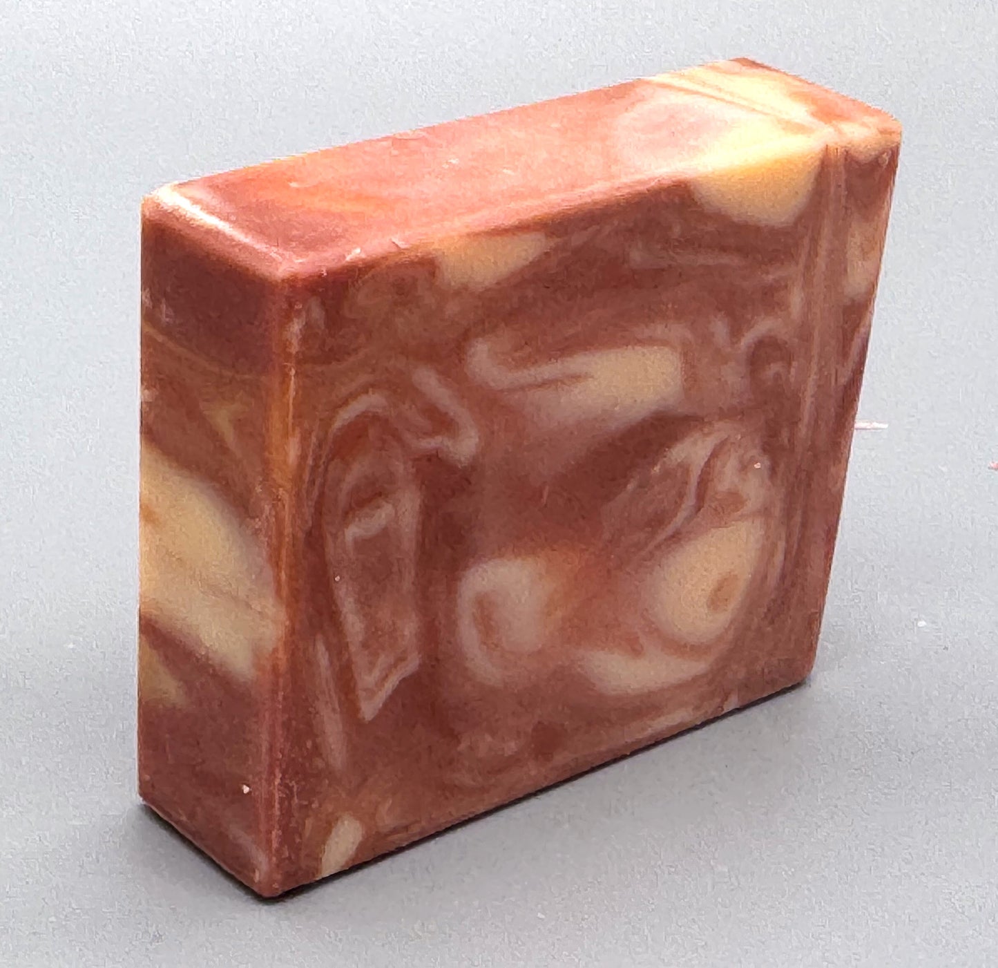 Handmade pink and cream swirled bar soap with warm, marbled tones, standing upright on a gray background